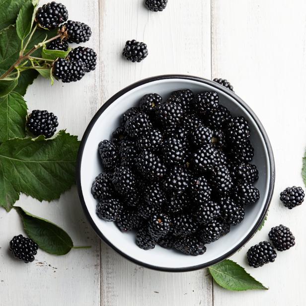Ein Schale voller Brombeeren auf einem weißen Holztisch.