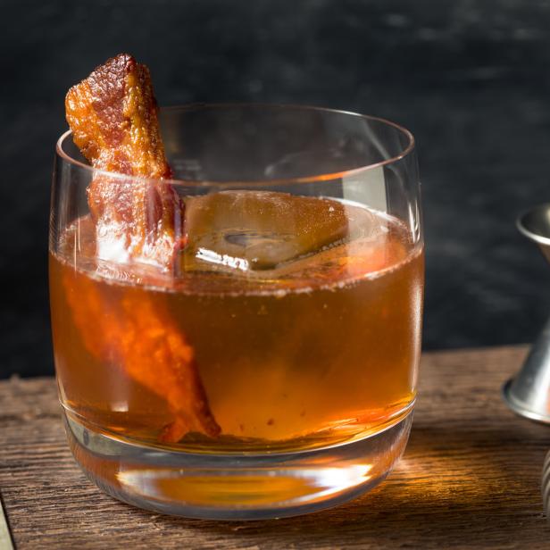 Ein Cocktail mit Eis und Speckgarnitur auf einem Holzbrett.