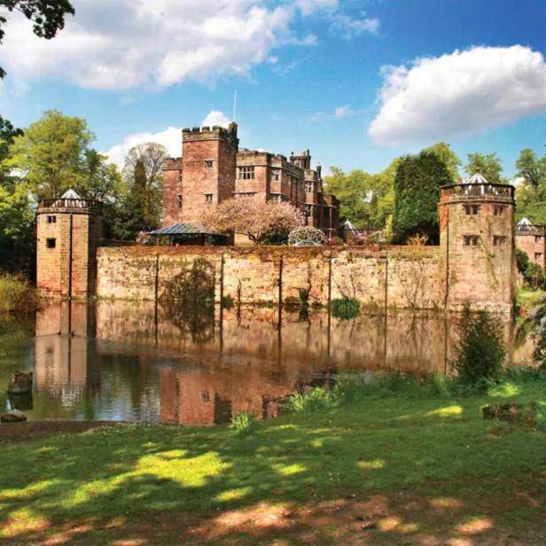 Ein von einem Wassergraben umgebenes Schloss aus rotem Backstein unter blauem Himmel.