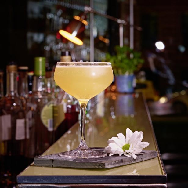Ein Cocktail in einem eleganten Glas steht auf einer Bar, dekoriert mit einer weißen Blüte.
