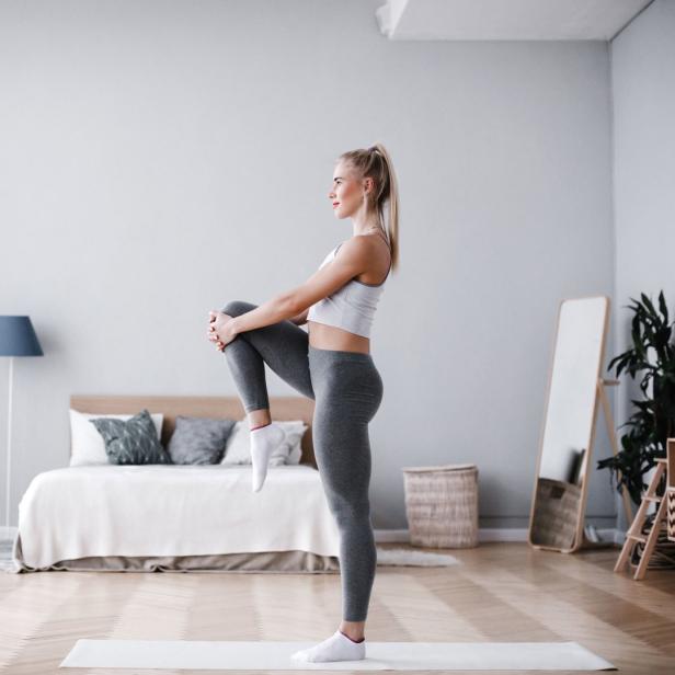 Eine Frau dehnt sich in einem hellen Raum auf einer Yogamatte.
