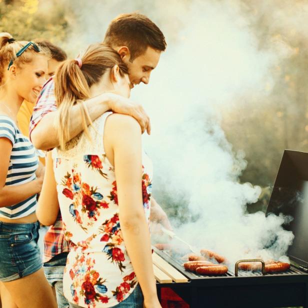 Eine Gruppe junger Leute grillt Würstchen im Freien.