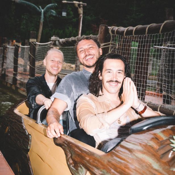 Drei Männer lachen in einem Baumstammboot auf einer Wasserbahn.