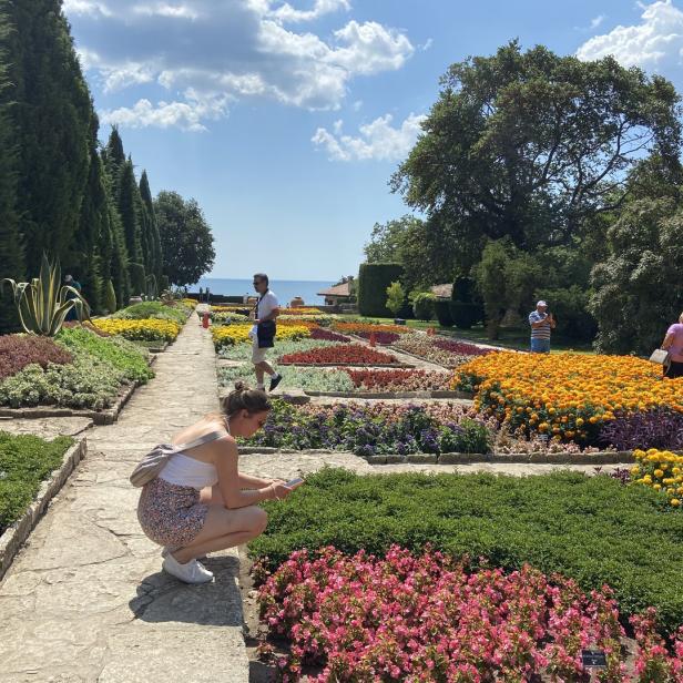 Eine Frau betrachtet Blumen in einem farbenprächtigen Garten am Meer.