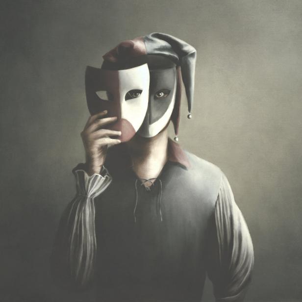 Eine Person mit Narrenkappe hält eine Maske vor ihr Gesicht.