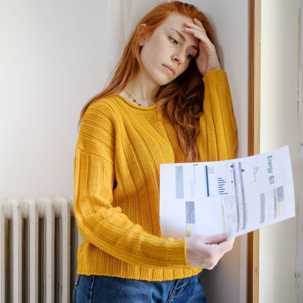 Eine Frau mit roten Haaren blickt besorgt auf ihre Energierechnung.