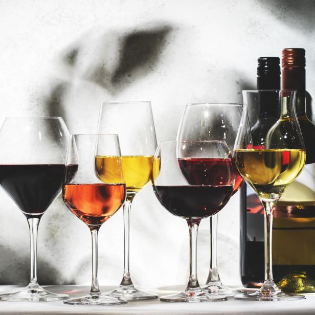 Mehrere Gläser mit Rotwein, Roséwein und Weißwein stehen vor Weinflaschen.