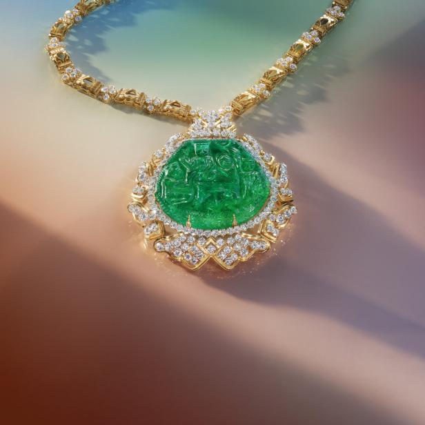 Eine goldene Halskette mit einem großen, geschnitzten Smaragdanhänger, umgeben von Diamanten.