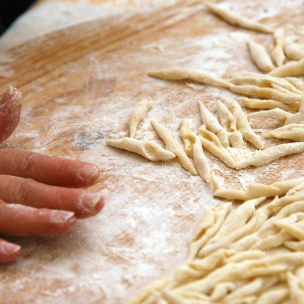 Eine Hand formt Trofie-Pasta auf einem bemehlten Holzbrett.