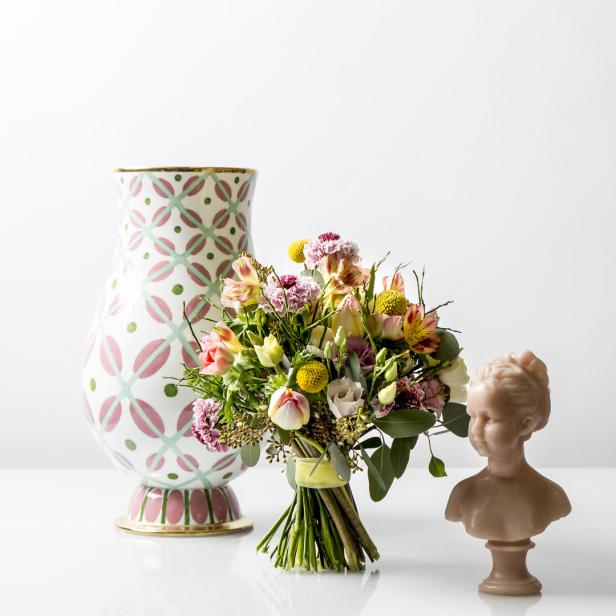 Ein Blumenstrauß steht neben einer verzierten Vase und einer kleinen Büste auf einem Tisch.