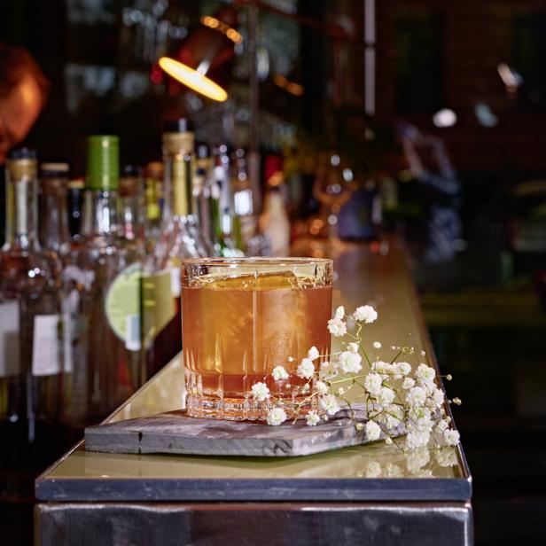 Ein Cocktail mit Eis und Orangenschale steht auf einer Bar, dekoriert mit Schleierkraut.