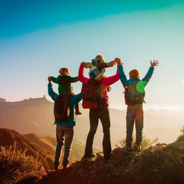 Eine Familie genießt die Aussicht von einem Berggipfel bei Sonnenuntergang.