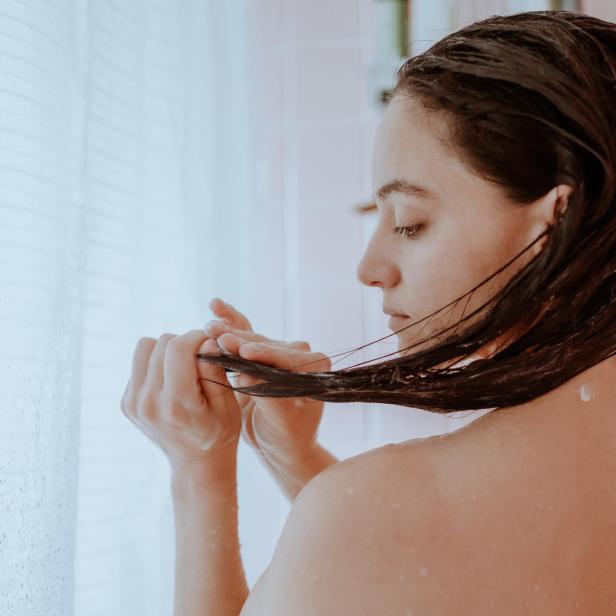 Eine Frau mit nassen, dunklen Haaren steht unter der Dusche.