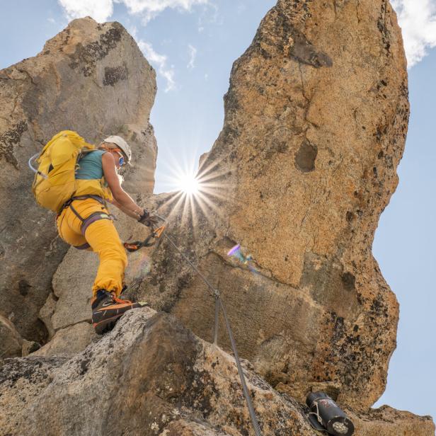 Eine Frau klettert mit gelbem Rucksack einen Felsen hinauf.