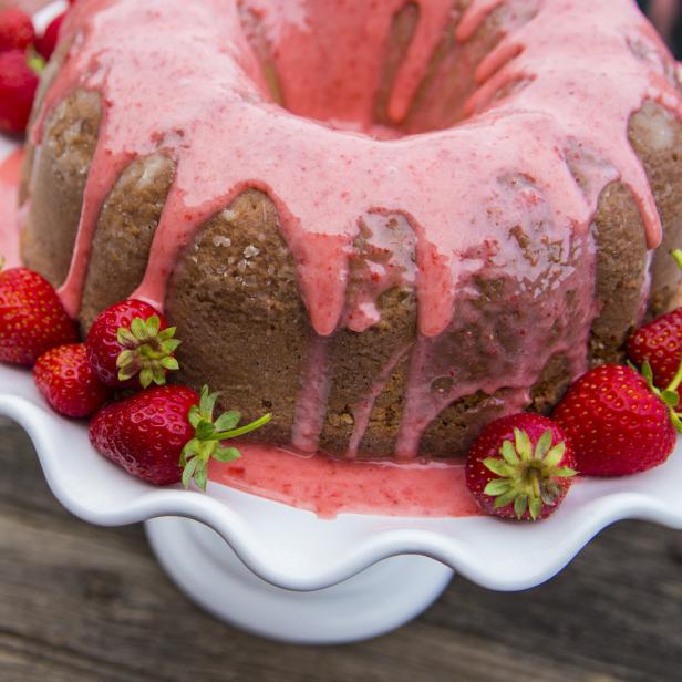 Ein Gugelhupf mit Erdbeerguss und frischen Erdbeeren auf einem weißen Teller.