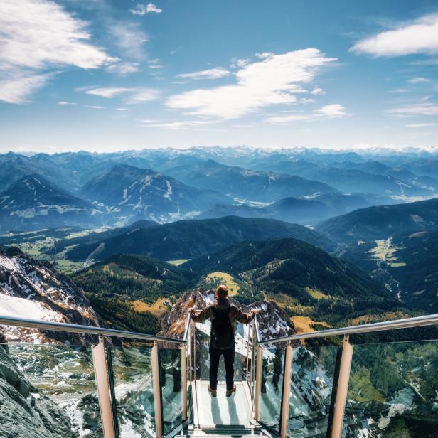 Ein Mann steht auf einer Aussichtsplattform und blickt auf die Berglandschaft.