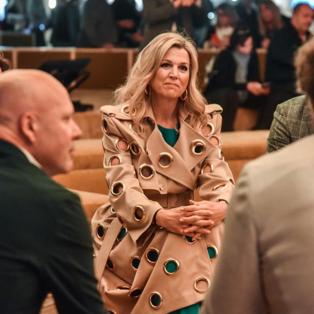 Königin Máxima trägt einen beigefarbenen Mantel mit goldenen Ösen.