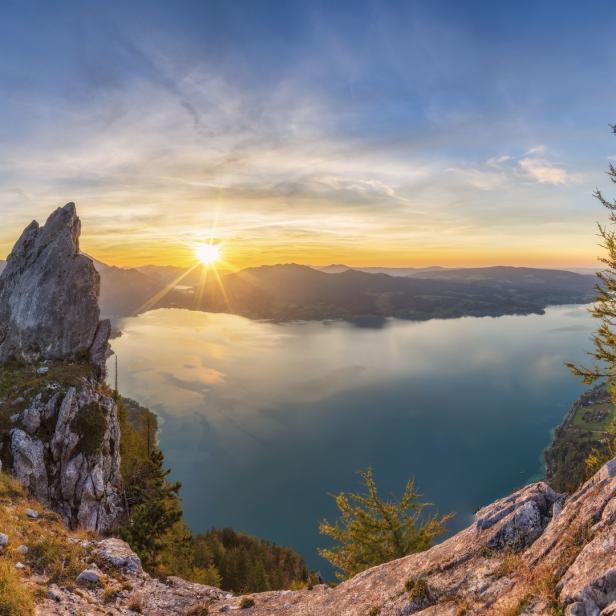 Sonnenaufgang über einem Bergsee, gesehen von einem felsigen Gipfel.