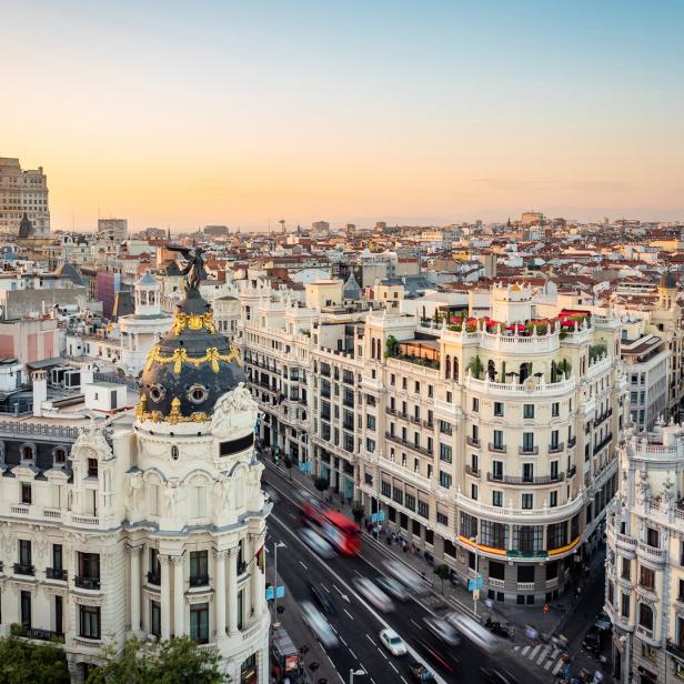 Blick auf die Skyline von Madrid bei Sonnenuntergang mit dem Metropolis-Gebäude im Vordergrund.