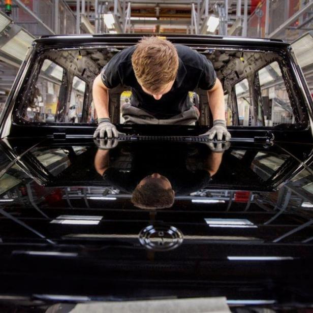 Ein Arbeiter montiert in einer Fabrik die Windschutzscheibe an einem schwarzen Fahrzeug.
