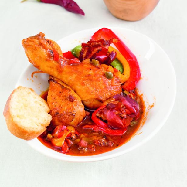 Hähnchenschenkel mit Paprika und Brot auf einem Teller angerichtet.