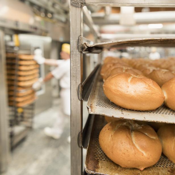 Ein Bäcker schiebt einen Wagen mit frischen Brötchen in einen Ofen.