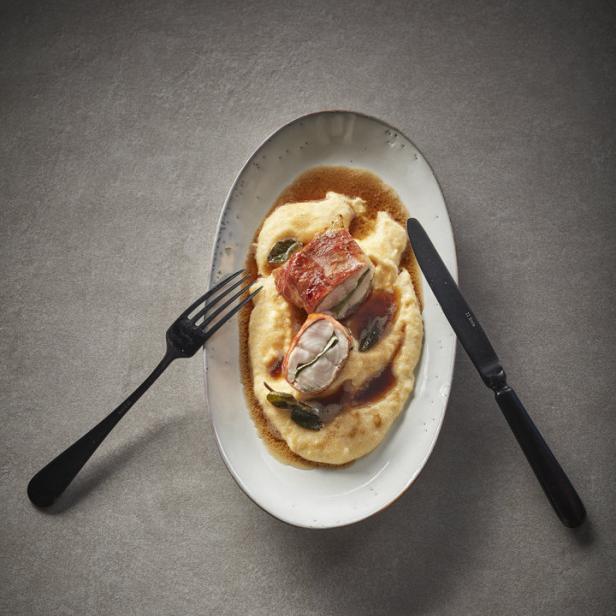 Auf einem Teller liegen Saltimbocca auf Polenta mit Salbei, dazu Messer und Gabel.