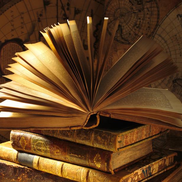 Ein aufgeschlagenes Buch liegt auf einem Stapel alter Bücher vor einer Weltkarte.