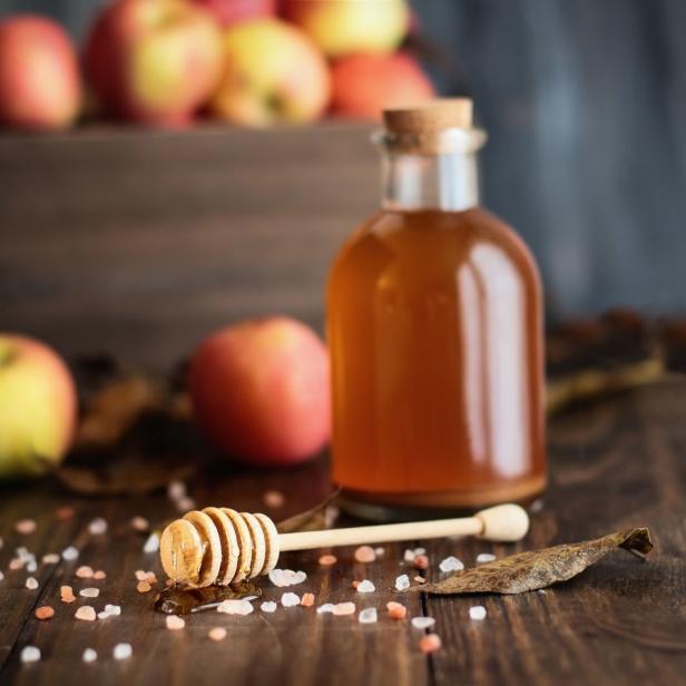 Apfelessig in einer Flasche mit Honig und Äpfeln im Hintergrund.