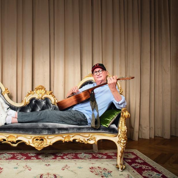 Ein Mann liegt auf einem verzierten Sofa und spielt Gitarre.