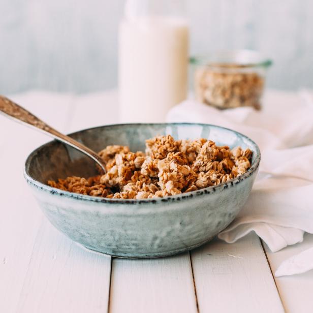Eine Schüssel Müsli mit einem Löffel auf einem weißen Holztisch.