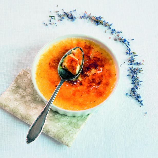 Eine Crème brûlée mit Lavendelblüten und einem Löffel auf einem Tisch.