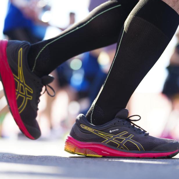 Ein Läufer mit schwarzen Socken und Asics-Laufschuhen auf einer Straße.