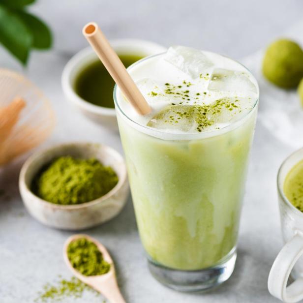 Ein Glas Matcha Latte mit Eis und ein Becher mit heißem Matcha-Tee stehen auf einem Tisch.
