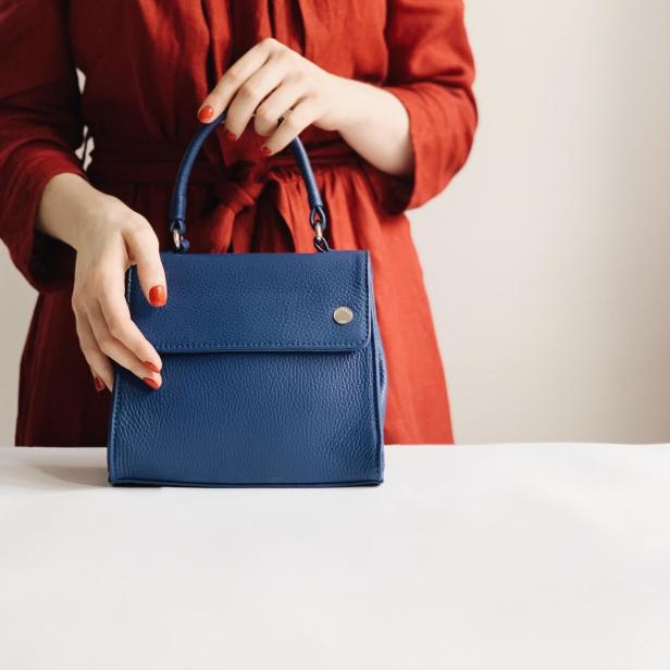 Eine Frau im roten Kleid hält eine blaue Ledertasche.