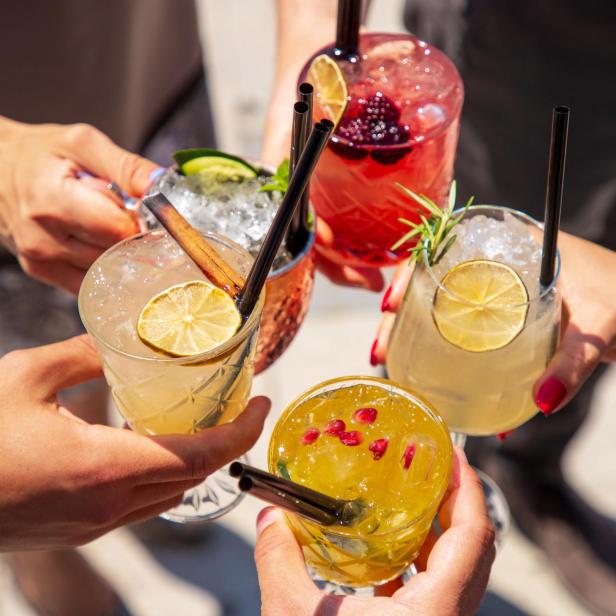 Mehrere Personen stoßen mit bunten Cocktails an.