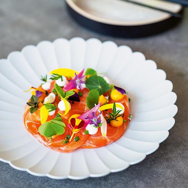 Ein Teller mit Lachscarpaccio, garniert mit Blüten und Kräutern.