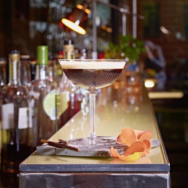 Ein Espresso Martini auf einer Bar, dekoriert mit einer Blüte und Schokostäbchen.
