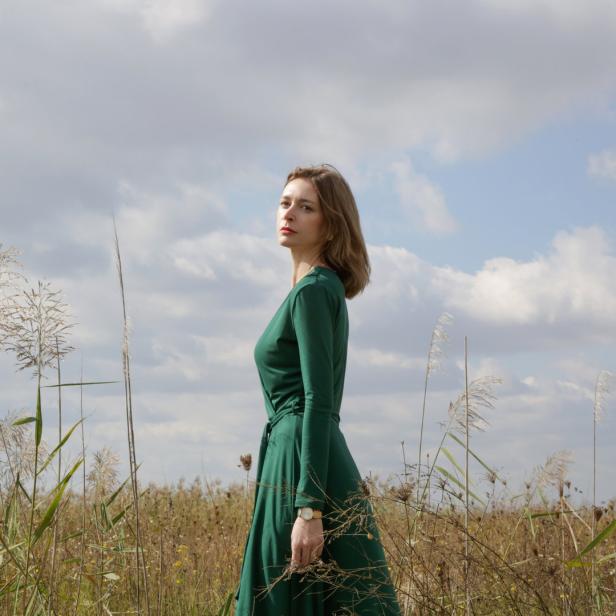Eine Frau in einem grünen Kleid steht in einem Feld mit hohem Gras.