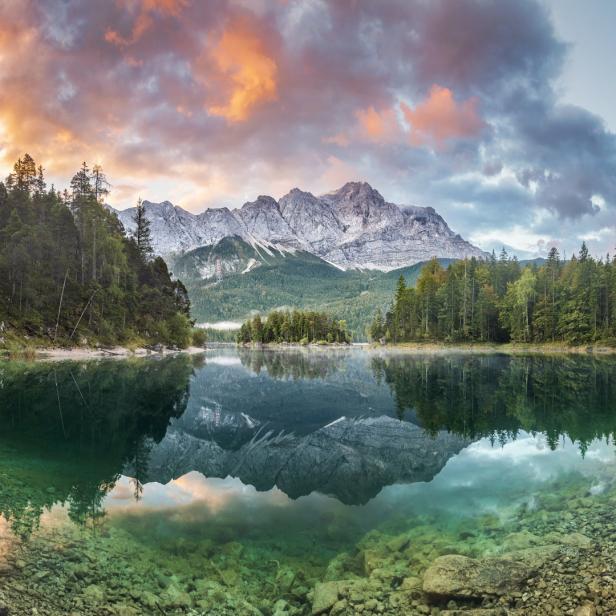 Der Eibsee spiegelt die Zugspitze und den bewaldeten Uferbereich wider.