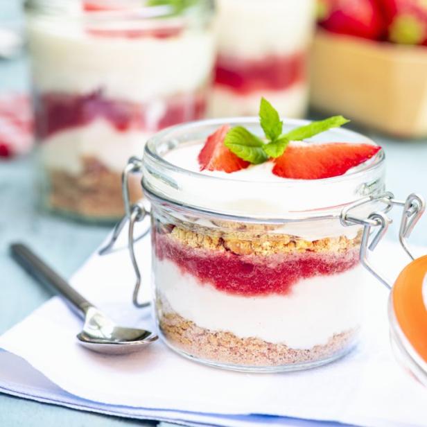 Ein Glas mit einem Dessert aus Erdbeeren, Joghurt und Keksstreuseln.