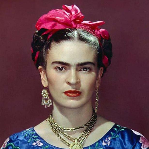 Ein Porträt von Frida Kahlo mit roter Blume im Haar und traditionellem Schmuck.