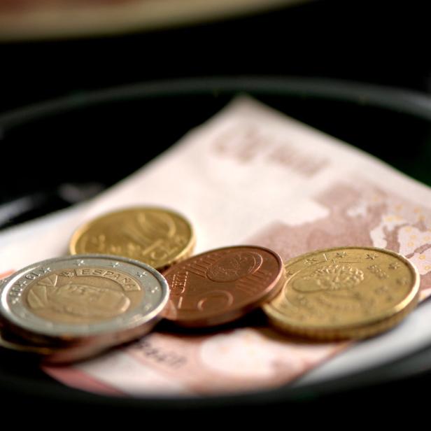 Eine 5-Euro-Note und ein paar Euro-Münzen liegen in einer schwarzen Schale.