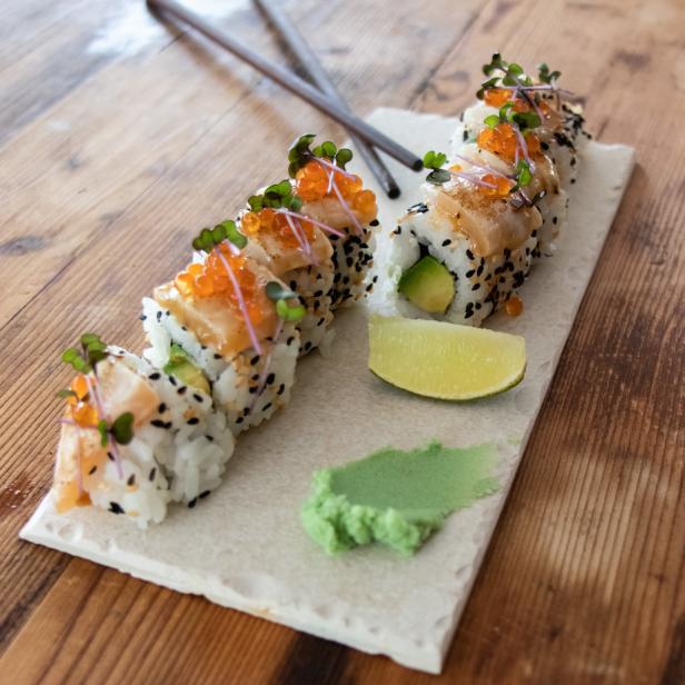 Eine Platte Sushi mit Lachs, Avocado, Wasabi und Limette, garniert mit Mikrogrün und Fischrogen.