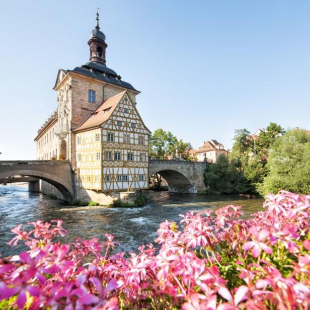 Das Alte Rathaus in Bamberg, malerisch auf einer Insel im Fluss gelegen, mit Blumen im Vordergrund.