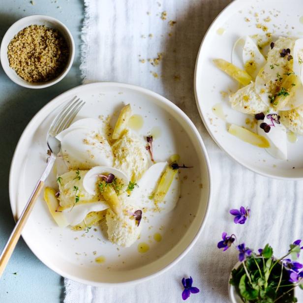 Zwei Teller mit Spargelsalat, garniert mit Veilchenblüten, auf einem Tisch.