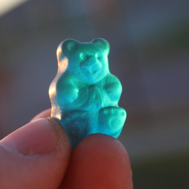 Ein blauer Gummibär wird von einem Finger gehalten.