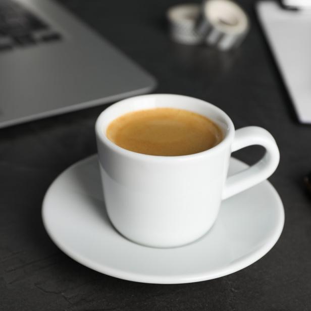 Eine Tasse Espresso steht auf einem Schreibtisch mit Laptop und Smartphone.