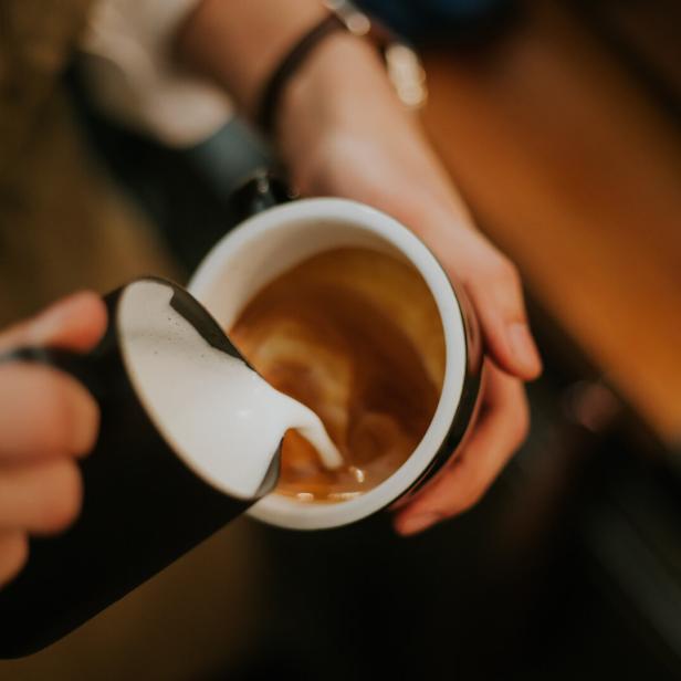 Jemand gießt Milch in eine Tasse Kaffee.