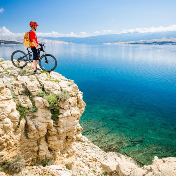 Ein Radfahrer steht mit seinem Mountainbike auf einer Klippe mit Blick auf das Meer.